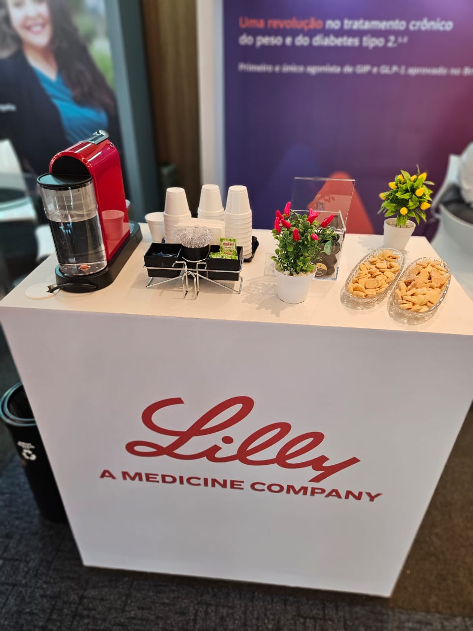 Bancada de coffee break com cafeteira, cápsulas, copos e snacks